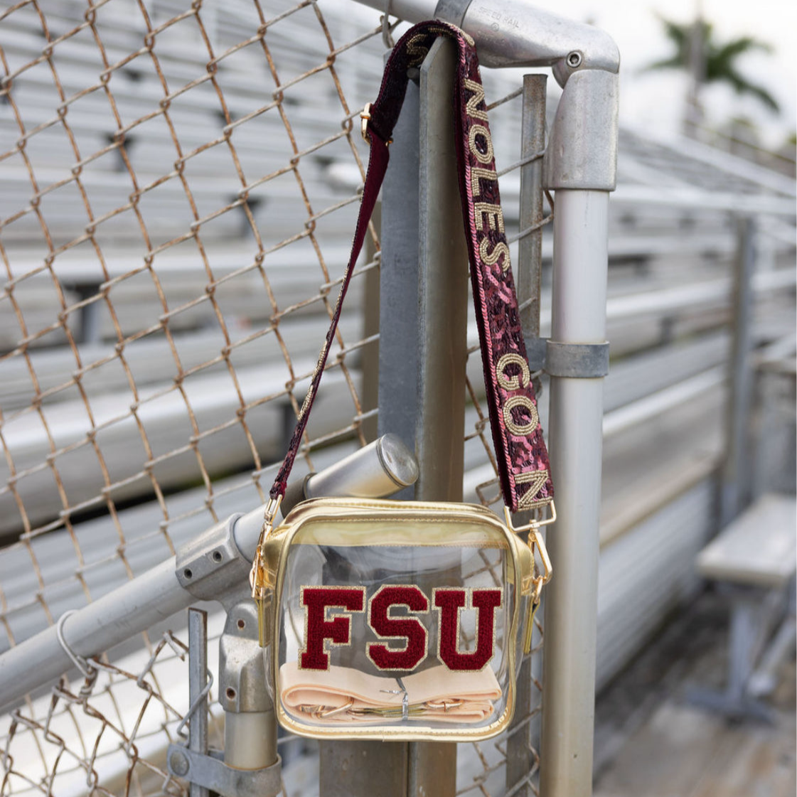 Clear handbag with 'FSU' text and red strap hanging on a metal railing.