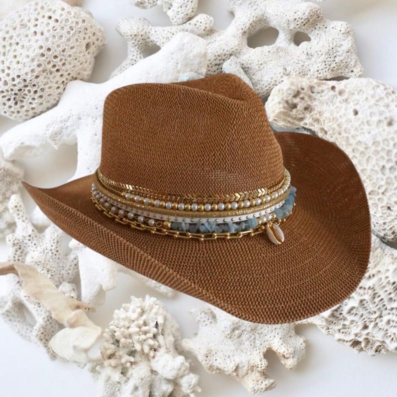 Luxury white cowgirl beach hat with shells and gold jewelry, handmade straw hat perfect for summer coastal resort wear.